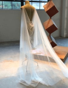 the lotus bloom company tulle drape back wedding cape on dress form in art studio in front of metal sculpture