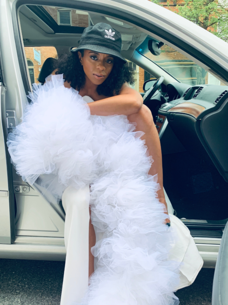 Keisha Ransome sitting in car wearing white tulle boa by the lotus bloom co and Adidas bucket hat.