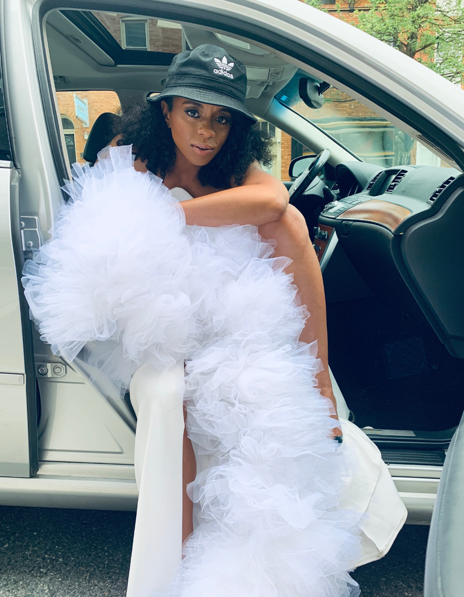 Keisha Ransome sitting in car wearing white tulle boa by the lotus bloom co and Adidas bucket hat.