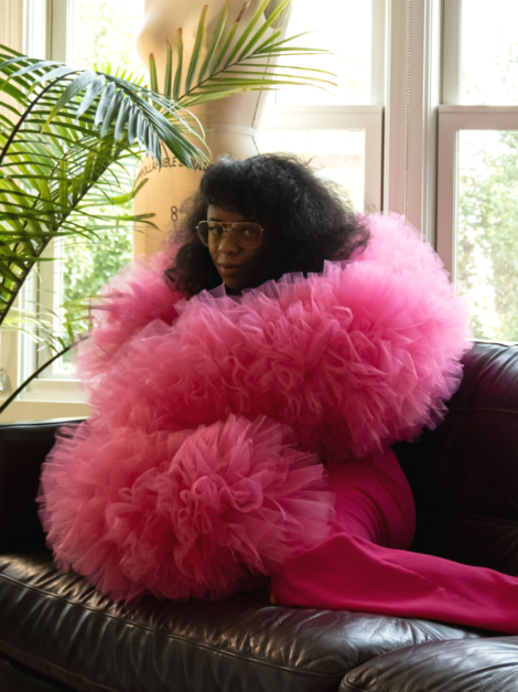 Keisha Ransome seated on sofa wearing a fuchsia pink tulle boa by the lotus bloom co.