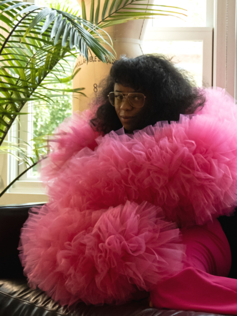 Keisha Ransome seated on sofa wearing a fuchsia pink tulle boa by the lotus bloom co.